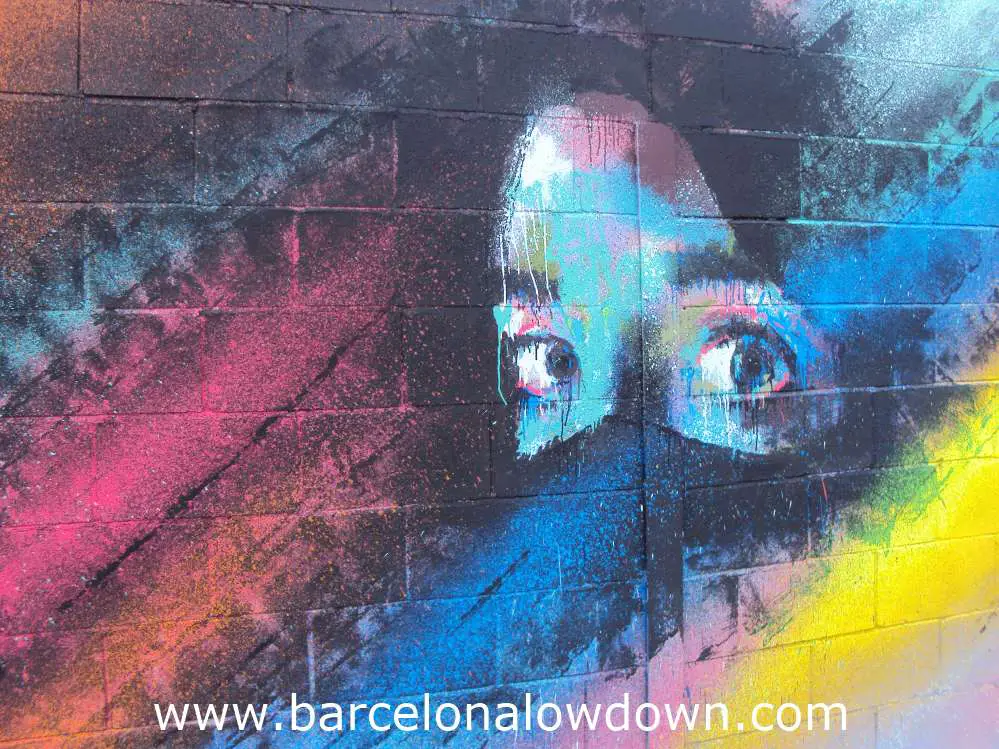 Painting of a girls eyes on a multicoloured black background, painted on a breezeblock wall.