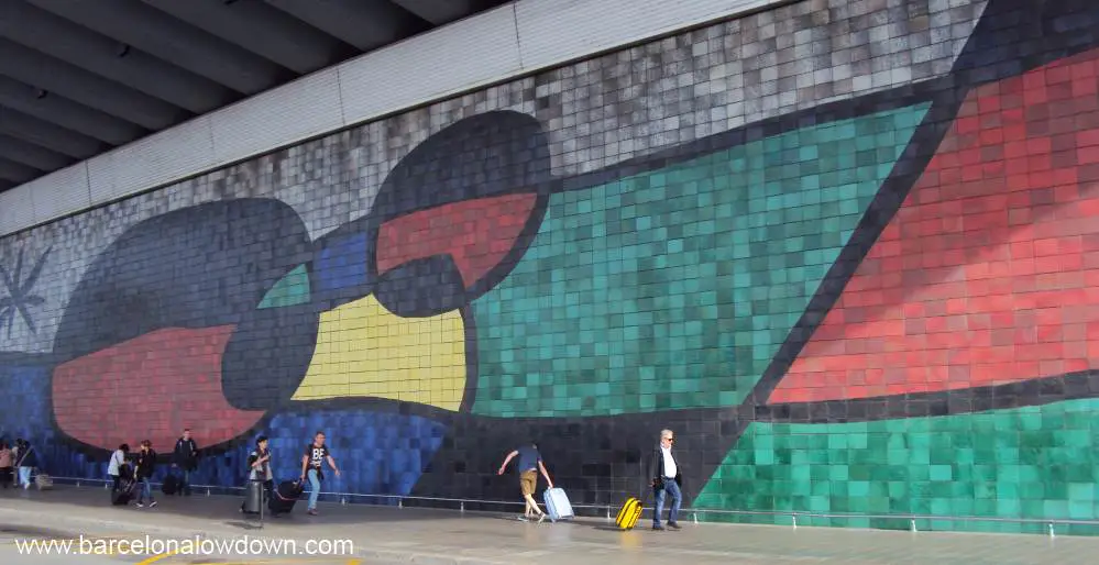 Tourists with suitcases walking in front of a giant tiled mural by Catalan artist Joan Miro