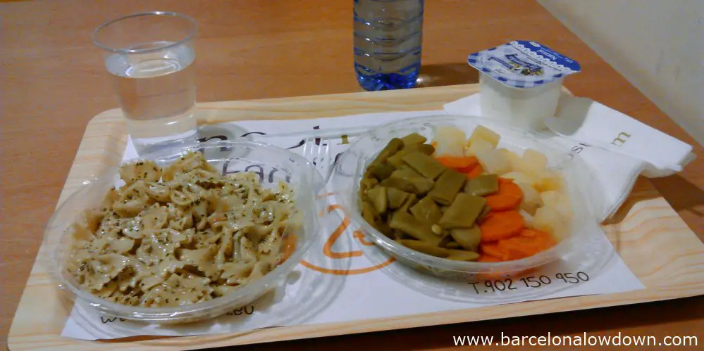 A tray of food at Nostrum Barcelona. The dishes are Pasta with pesto sauce, mixed steamed vegetables and natural yogurt washed down with a bottle of water.
