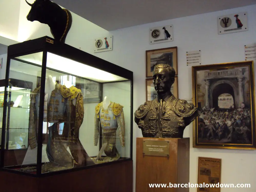 A bronze statue of famous Spanish bullfighter Manolete, 2 bullfighters' costiumes in a glass cabinet, a stuffed bulls' head and various old photos in the bullfighting museum located in the Plaza de Toros Monumental bulring Barcelona, Spain