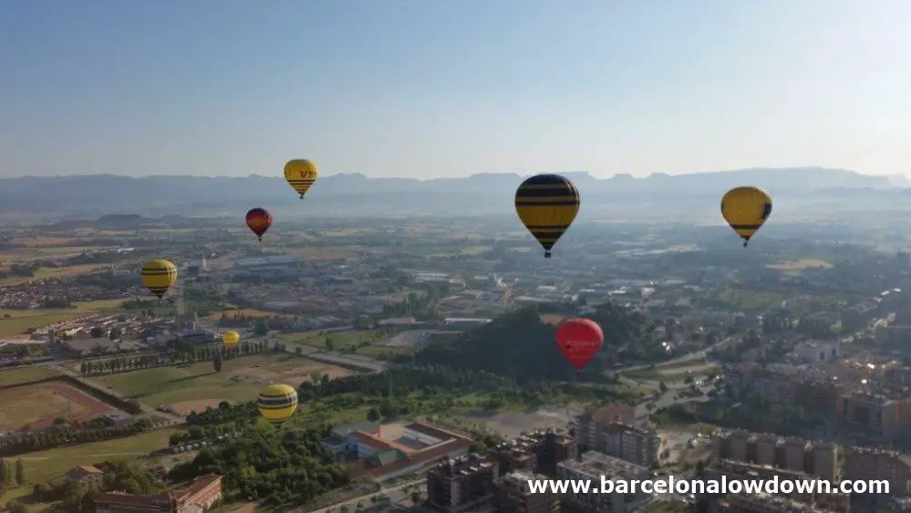 8 colorful hot air balloons slowly rising over the city of Vic near Barcelona with distant views of the Catalan mountains too the north.