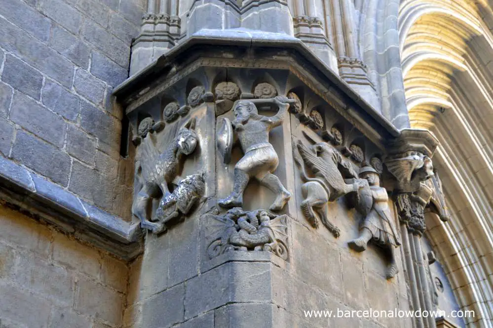 Stone carving of Wilfred the Hairy slaying a dragon with a wooden staff next to the door of Barcelona cathedral