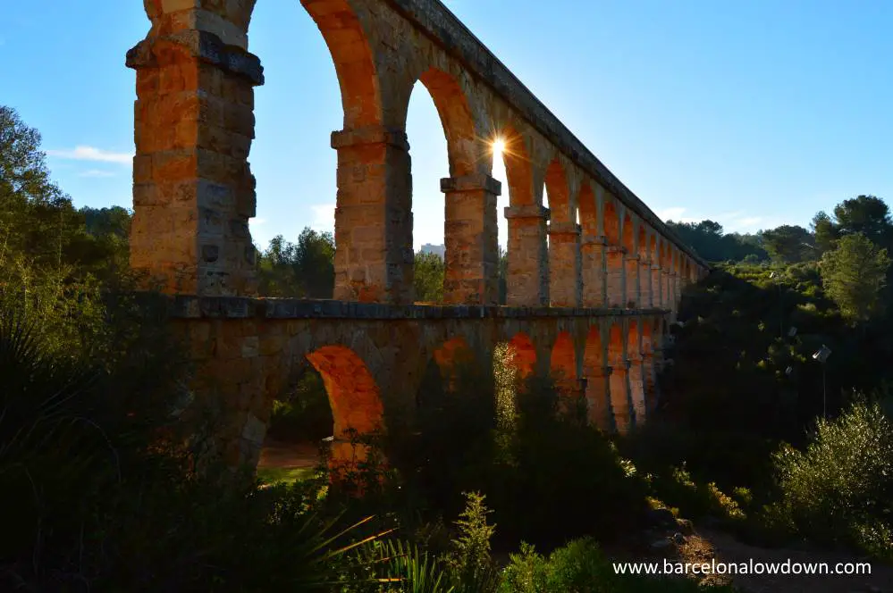 Photo of the Roman aqueduct near Tarragona, Spain. The photo was taken early in the morning and the sun shines between the arches of the aqueduct.