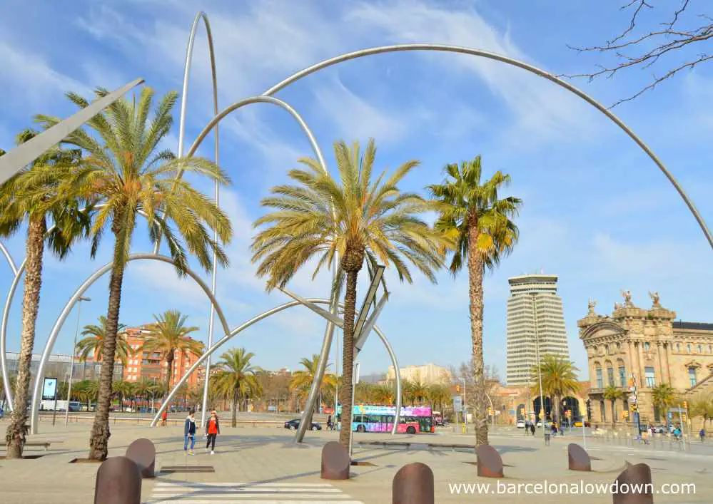 Photo of Andreu Alfaro's waves statue taken on a sunny day in February in Barcelona. You can see the Barcelona custom house, the Maritime Museum and an open top tour bus in the background.