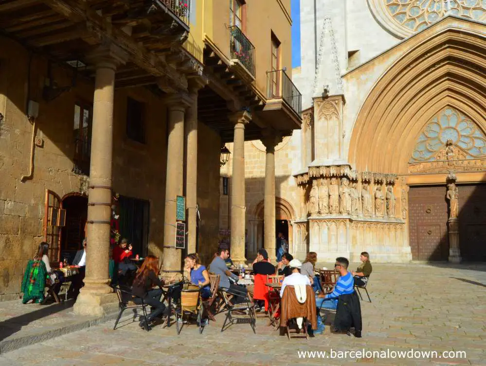 People drinking and talking on a busy terrace in front of Tarragona Cathedral