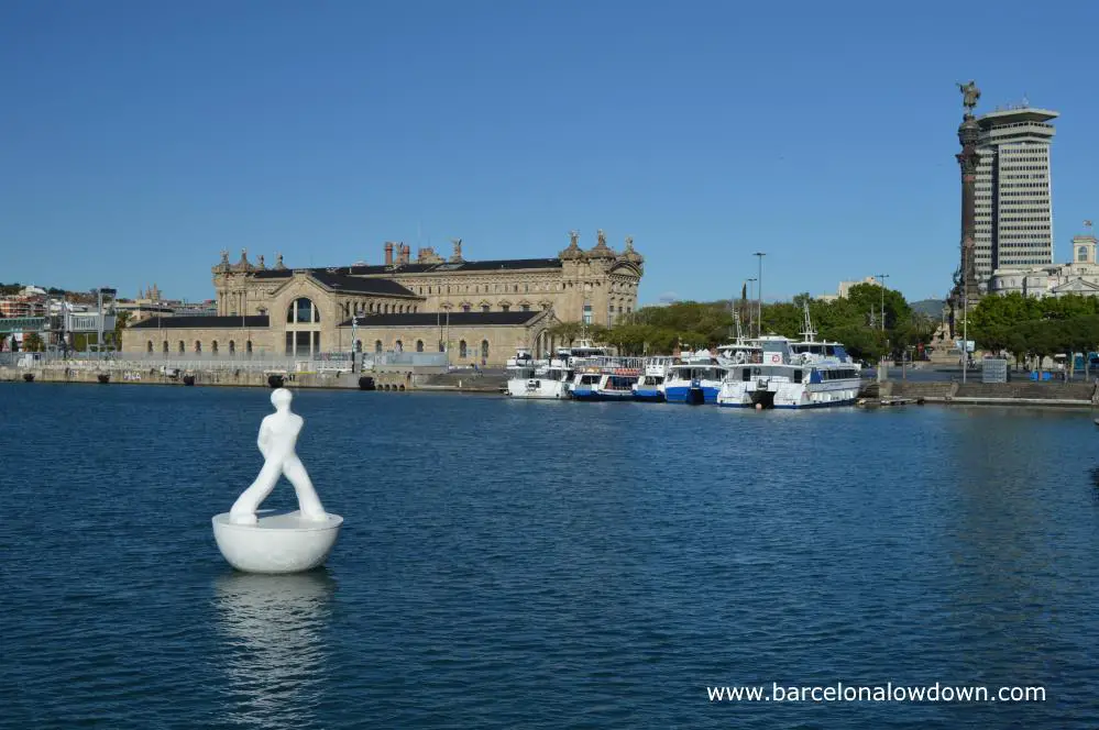 One of the white stargazer statues in front of the Columbus monument and the old harbour buildings of Barcelona's Port Vell