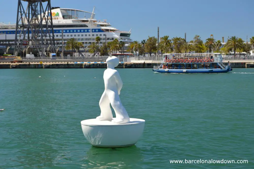 One of the two white figures which make up the mirsestels or stargazer monument in the old harbour, Barcelona. In the background you can see a cruise ship and one of the small boats which do harbour tours.