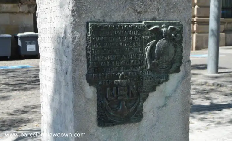 The metal plaque on the side of the monument to us servicemen in Barcelona. The design includes an eagle atop a globe and an anchor with the letters USN.