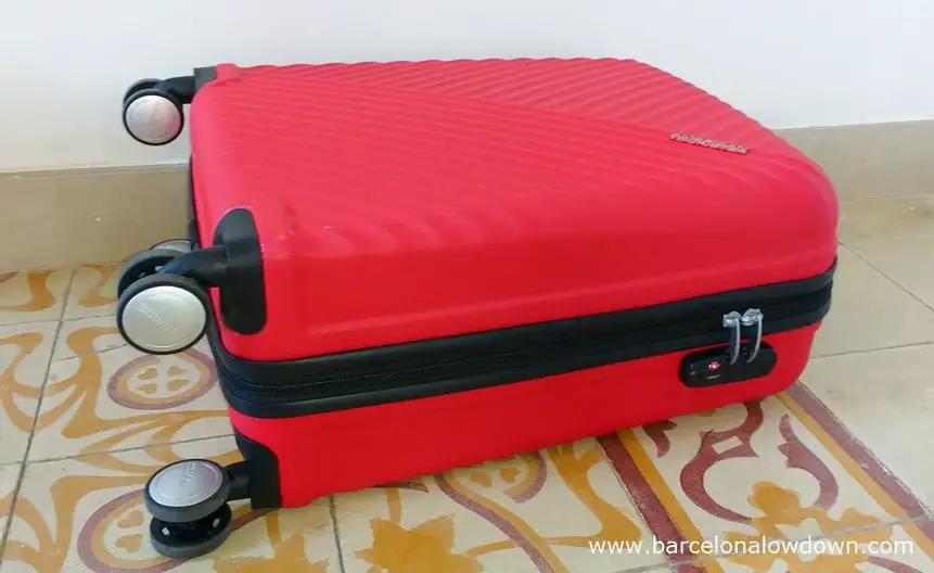 A red hand luggage size American Tourister suitcase with a built in combination lock