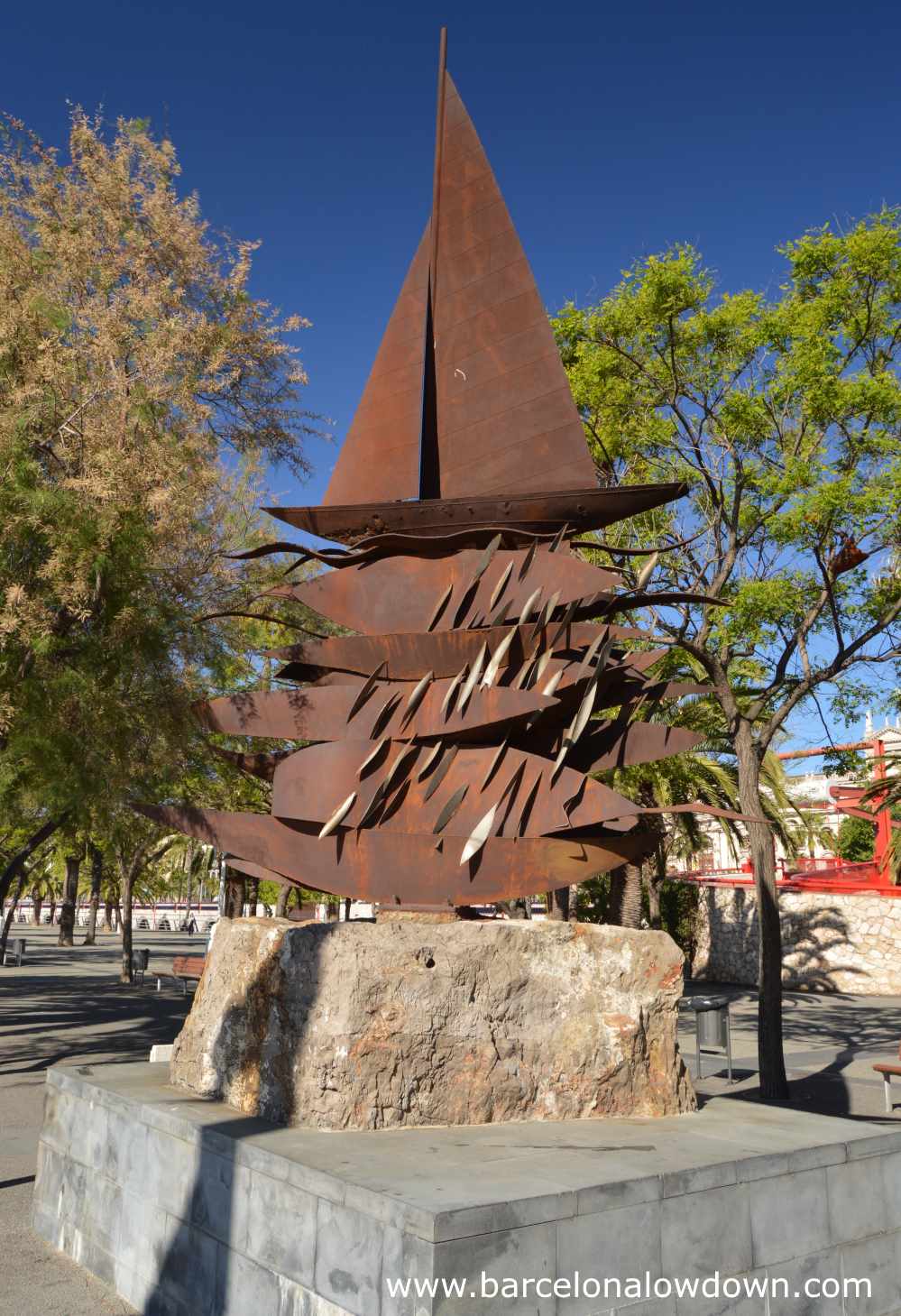 Rusty steel monument of a sailboat and giant fish at Barcelona's Port Vell marina.