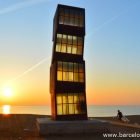 The wounded star statue at sunrise by Rebecca Horn. Photo of Barcelona beach, the early morning sunshine is shining through windows of thye rusty iron block statue staining them yellow. A lone paddlesurfer is walking across the sand carring their board towards the sea for an early morning surf session,