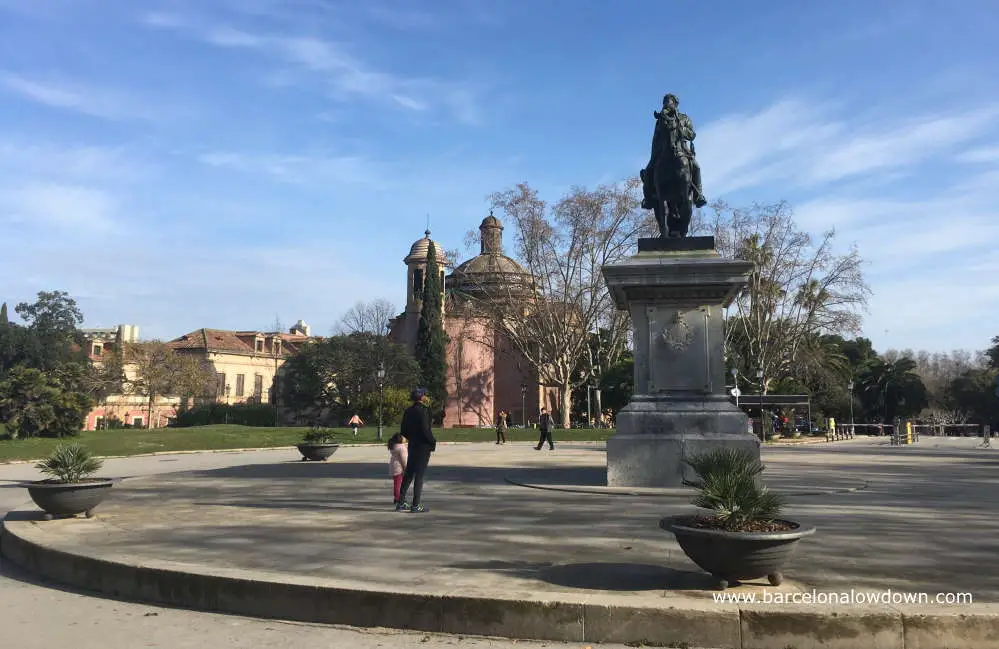 Two people looking at a statue of Joan Prim in the Citadel Park with the Military Parish Church in the background