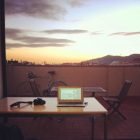 Ben Holbrook's desk on a roof terrace in Barcelona, his laptop and camera are on the desk and the sun is setting in the background