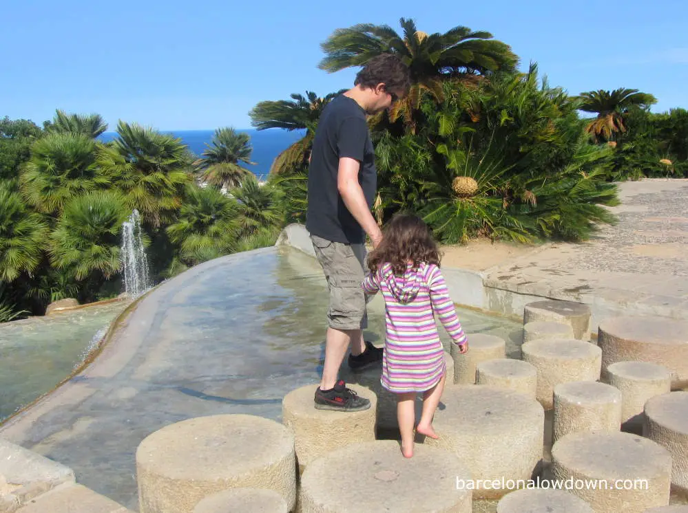 Father and child walking across stepping stones in the park near Barcelona Montjuic castle