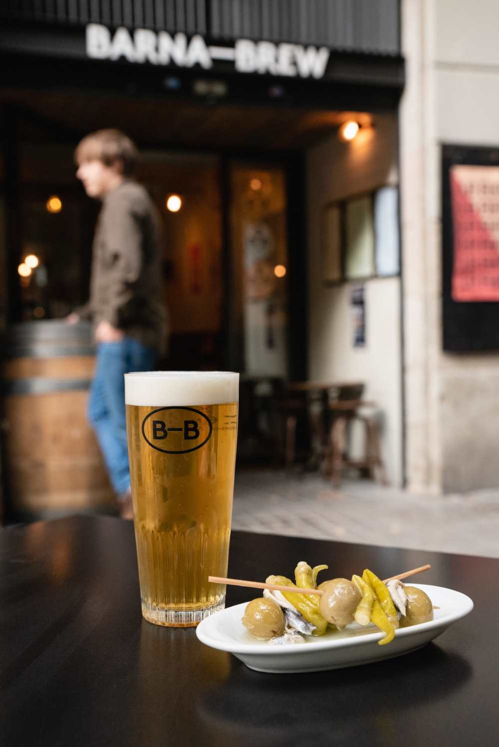 A glass of beer and some green olives on a table outside Barna Brew
