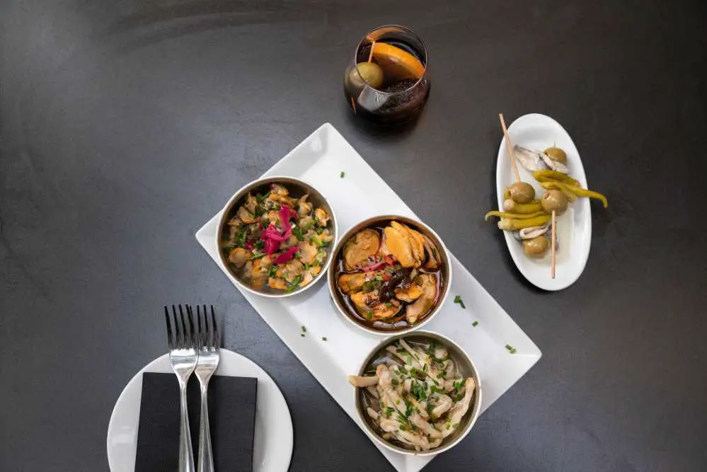 Assorted tapas and vermouth served on white plates on a black tabletop