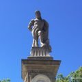 A stone statue of Hercules, standing on a pedestal with a large club in his hand