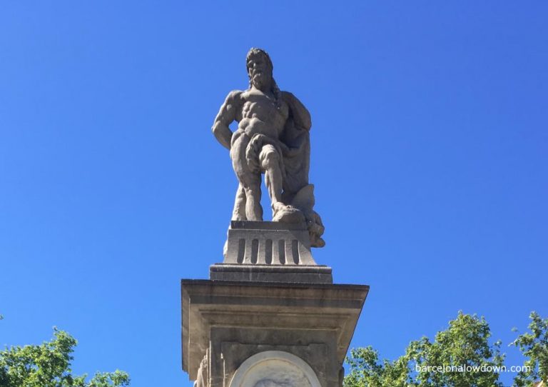 A stone statue of Hercules, standing on a pedestal with a large club in his hand