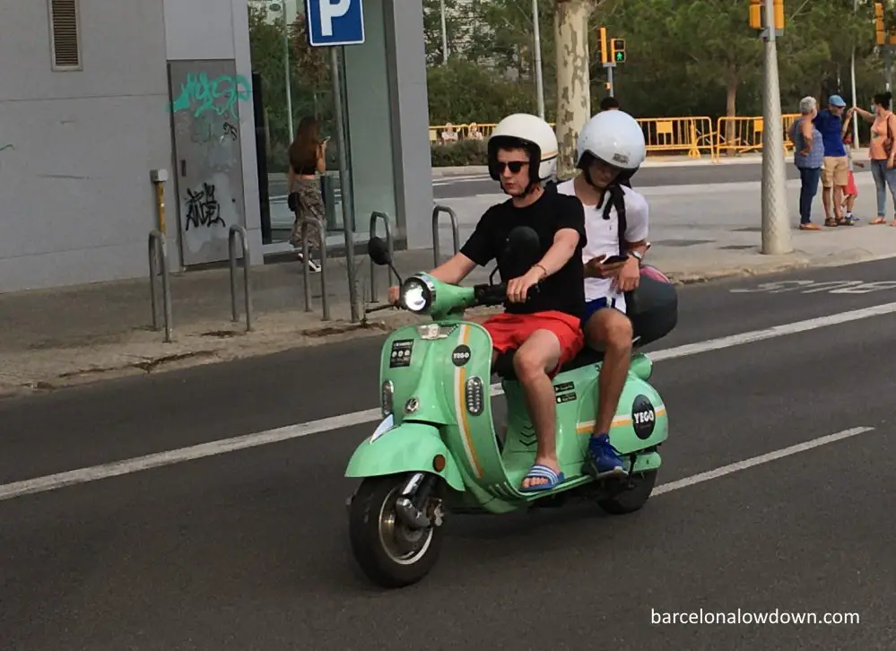 Two people riding a green electric moped in Barcelona