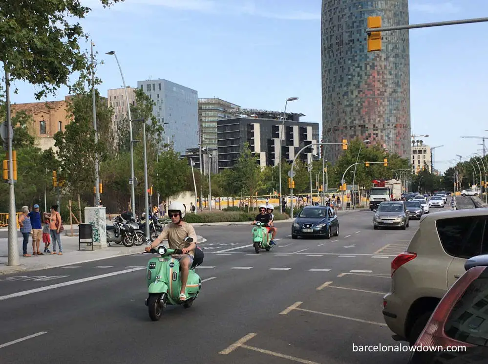 Two green electric scooters riding on the road near the Agbar Tower in Barcelona