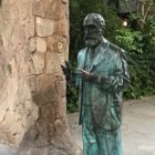 Bronze statue of Antoni Gaudí standing in front of a modernist style gateway in Barcelona