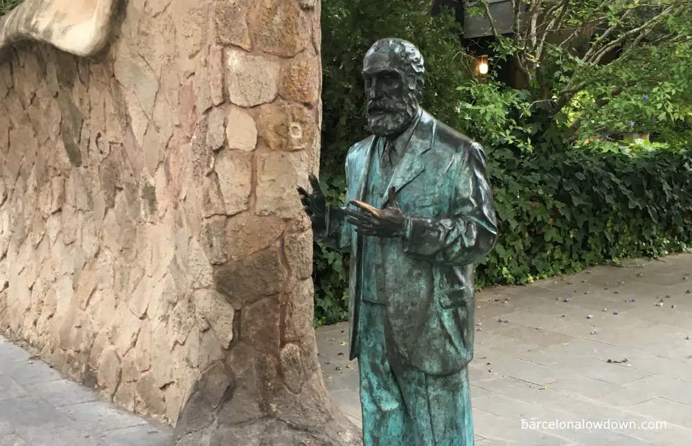 Bronze statue of Antoni Gaudí standing in front of a modernist style gateway in Barcelona