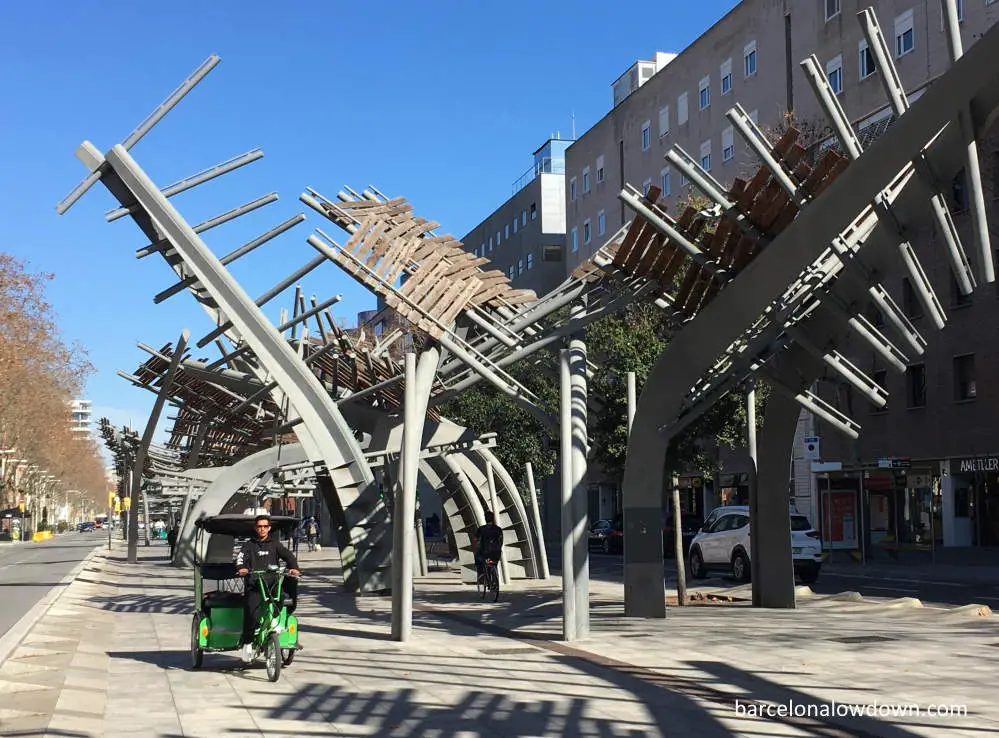 A rickshaw driver pedals past the steel pergolas on Icària Av. Barcelona, Spain